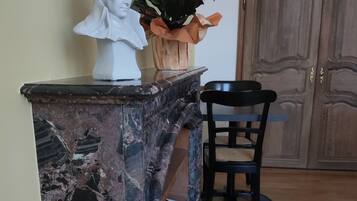A marble countertop with a bust sculpture, a potted plant, and a black chair in a room with wooden flooring and a wooden door.