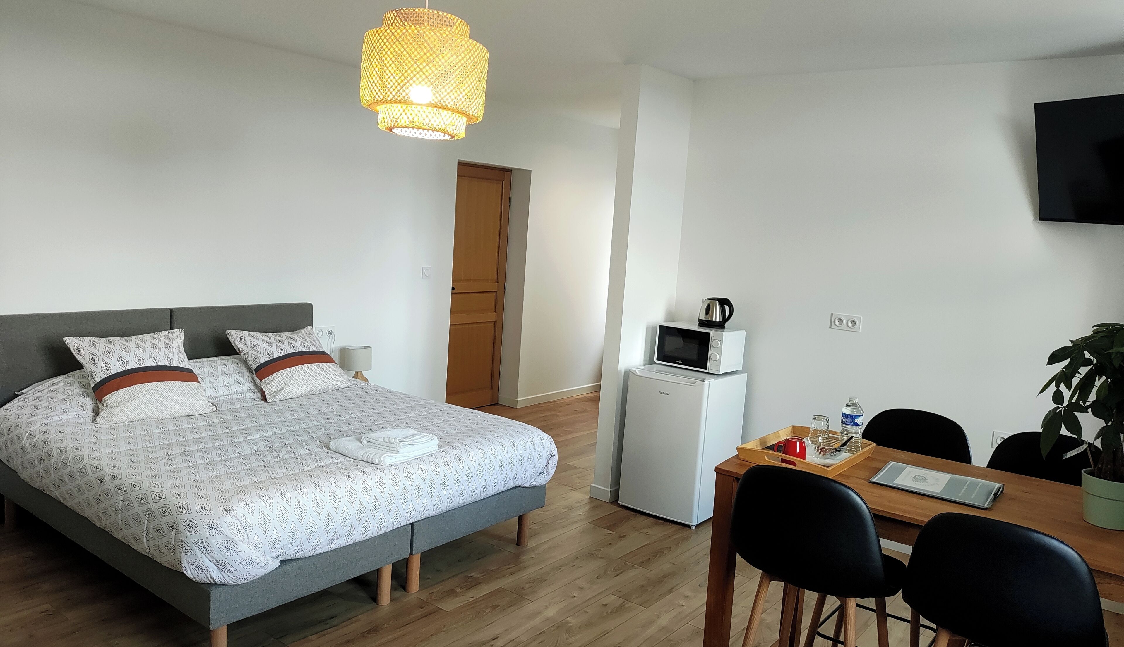 A bedroom with a bed, bedside table, lamp, and a small kitchenette with a microwave and kettle.