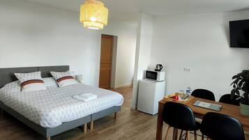 A bedroom with a bed, bedside table, lamp, and a small kitchenette with a microwave and kettle.