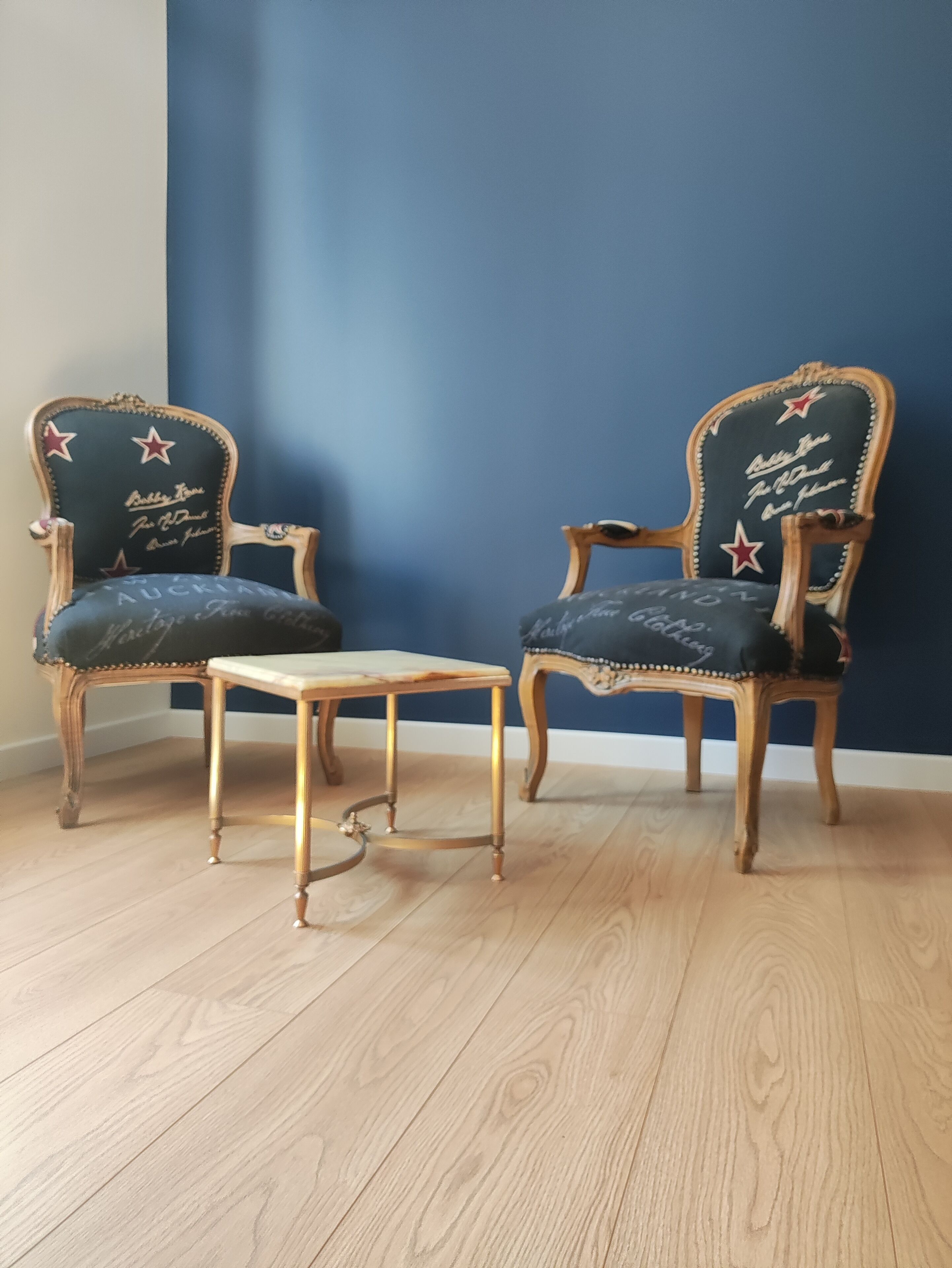 Zwei Stühle im Vintage-Stil mit Sternenverzierung und ein kleiner Holztisch in einem Raum mit Holzboden und blauer Wand.