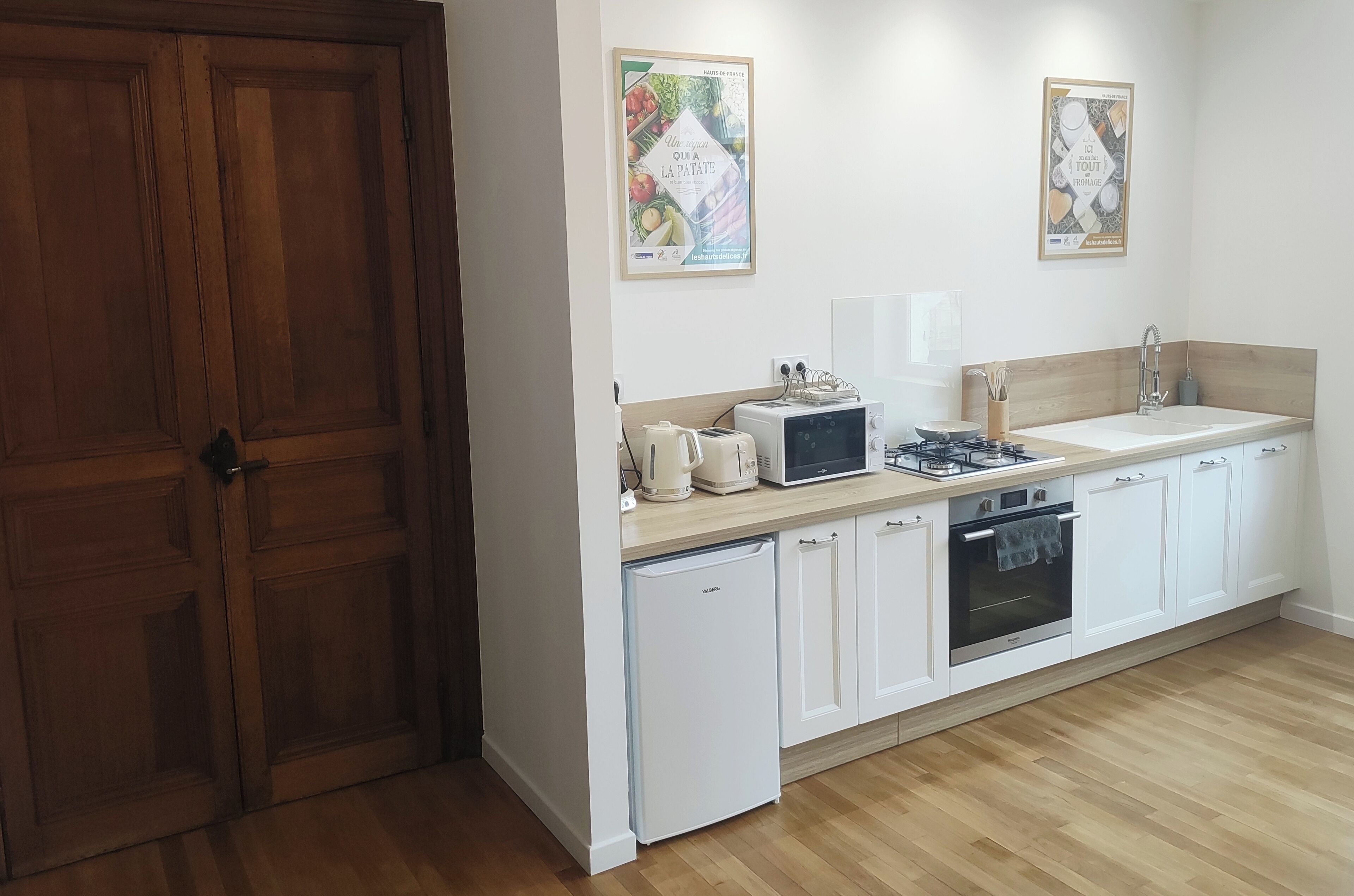A modern kitchen with white cabinets, a built-in oven, a microwave, and a sink. There are two framed posters on the wall.
