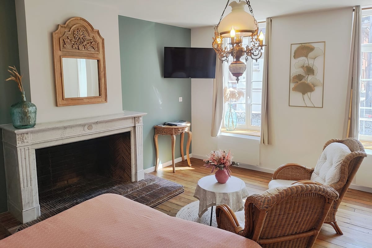 A cozy room with a fireplace, wicker chairs, a television, and a window with a view.