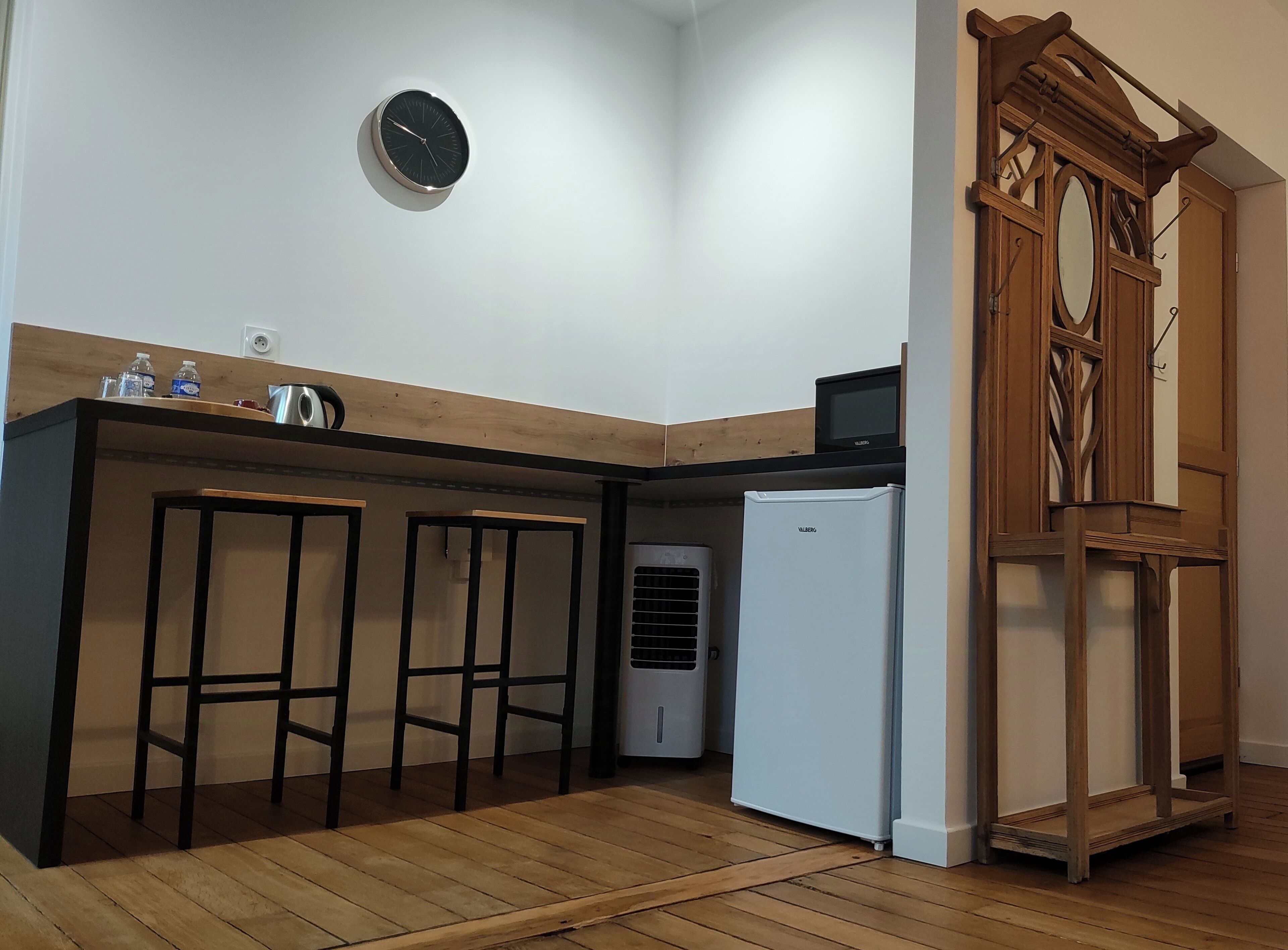 Een kleine keuken met een houten aanrecht, een witte koelkast, een wandklok en een houten stoel.