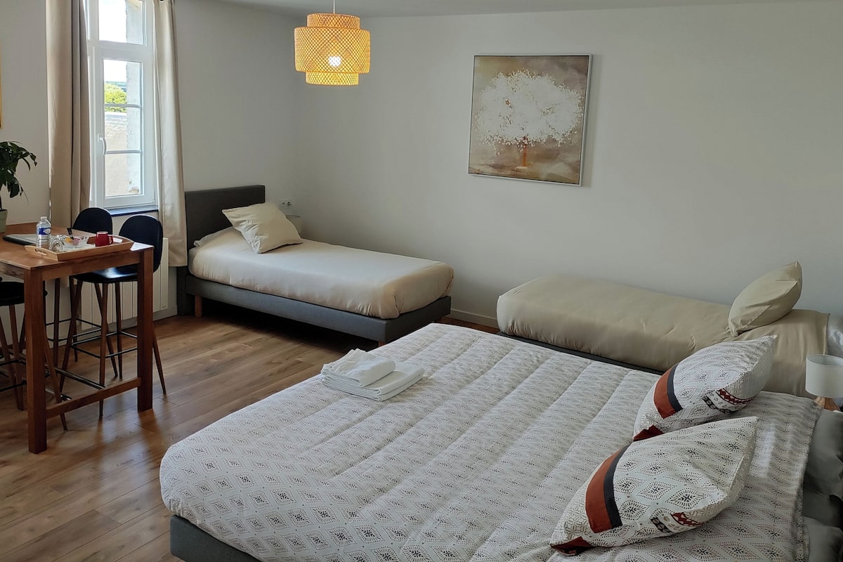 A bedroom with a bed, two smaller beds, a desk, a chair, a potted plant, and a painting on the wall.
