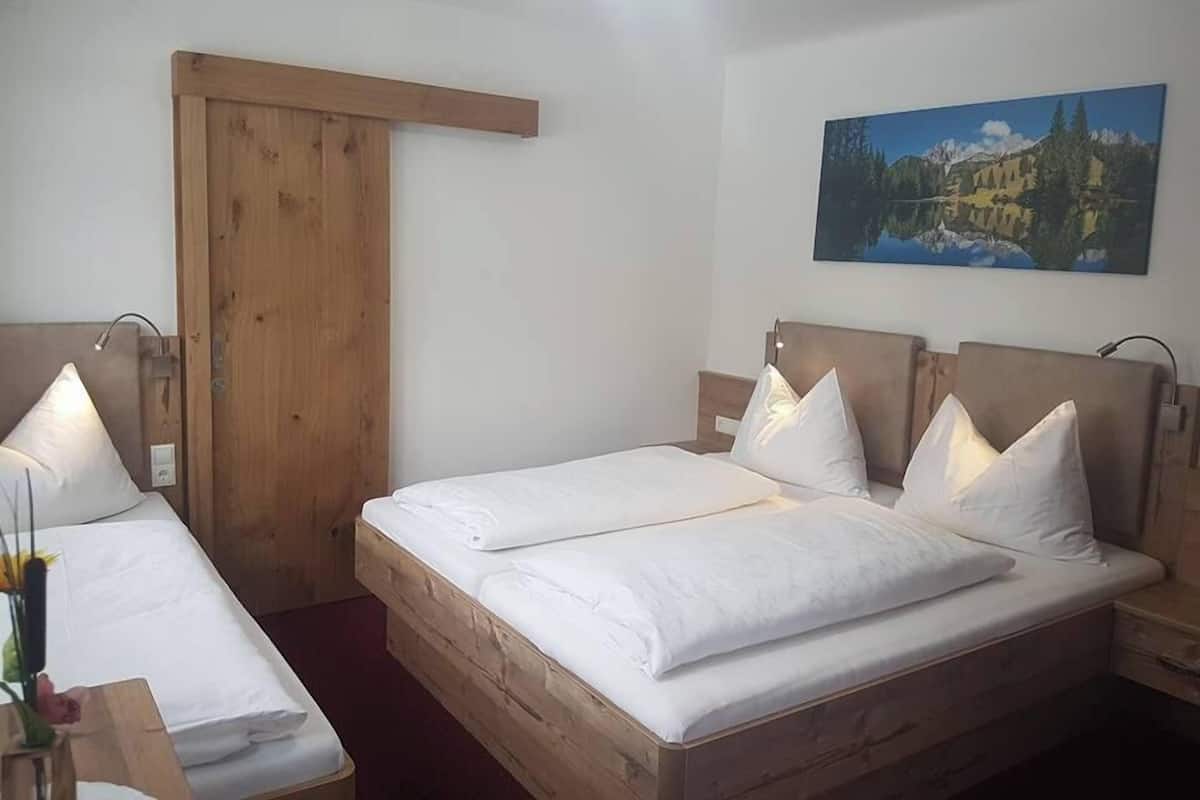 A hotel room with two single beds, wooden headboards, white bedding, a wooden door, and a painting of a landscape on the wall.