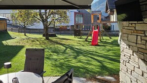 A patio area with a table and chairs, a children's play structure, and a view of a mountain and houses in the background. - No1 - Flo's modern Rooms & Breakfast  (Wagrain)