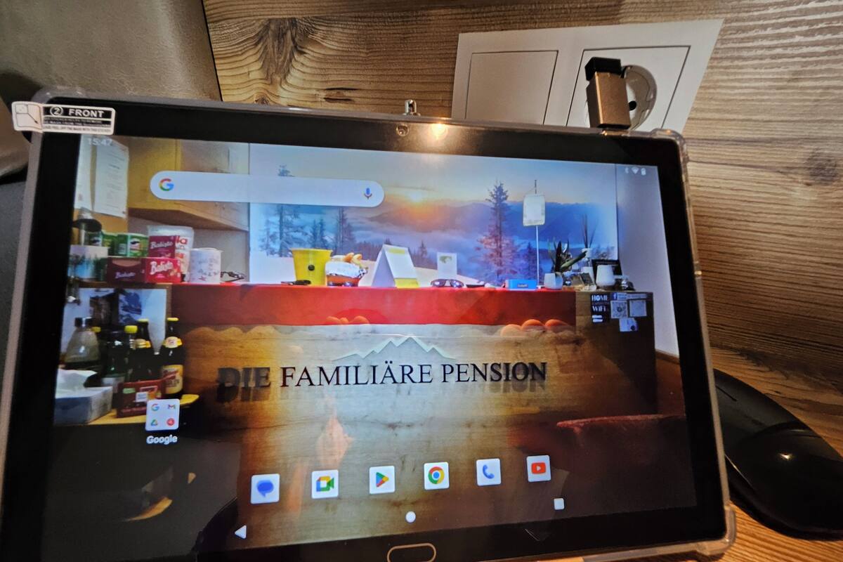 A tablet displaying a webpage with the text "Die Familien Pension" and various app icons.