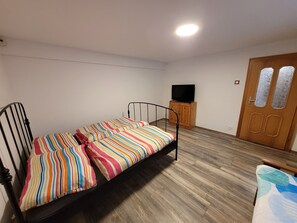 A single bed with a colorful striped bedspread, a wooden cabinet with a television, and a wooden door with frosted glass panels. - SELF-Check-In, 3 km from the highway (Wolfpassing an der Hochleithen)