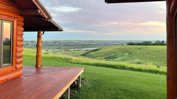 Une cabane en bois dotée d’une terrasse offrant une vue sur un paysage verdoyant et une rivière.