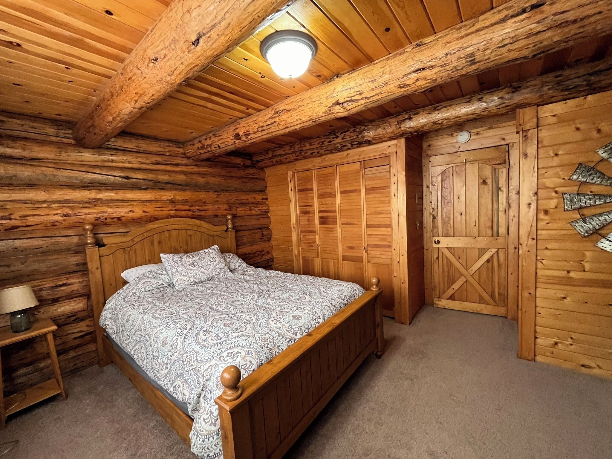 Un dormitorio de cabaña de madera con una cama de madera, una mesita de noche, un armario y una puerta con un diseño de cruz.