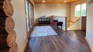 Une pièce spacieuse avec un plafond en bois, un plancher en bois foncé, une grande fenêtre et un banc intégré.