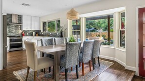 Una cocina moderna con armarios blancos, estufa integrada y comedor con mesa de madera y sillas estampadas.
