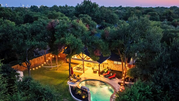 Una piscina de forma singular rodeada por una terraza, un área de estar al aire libre techada y un edificio de piedra con un patio.
