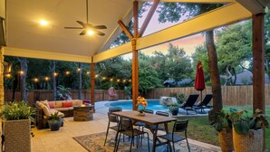 Un patio cubierto con piscina, mobiliario exterior e iluminación colgante.