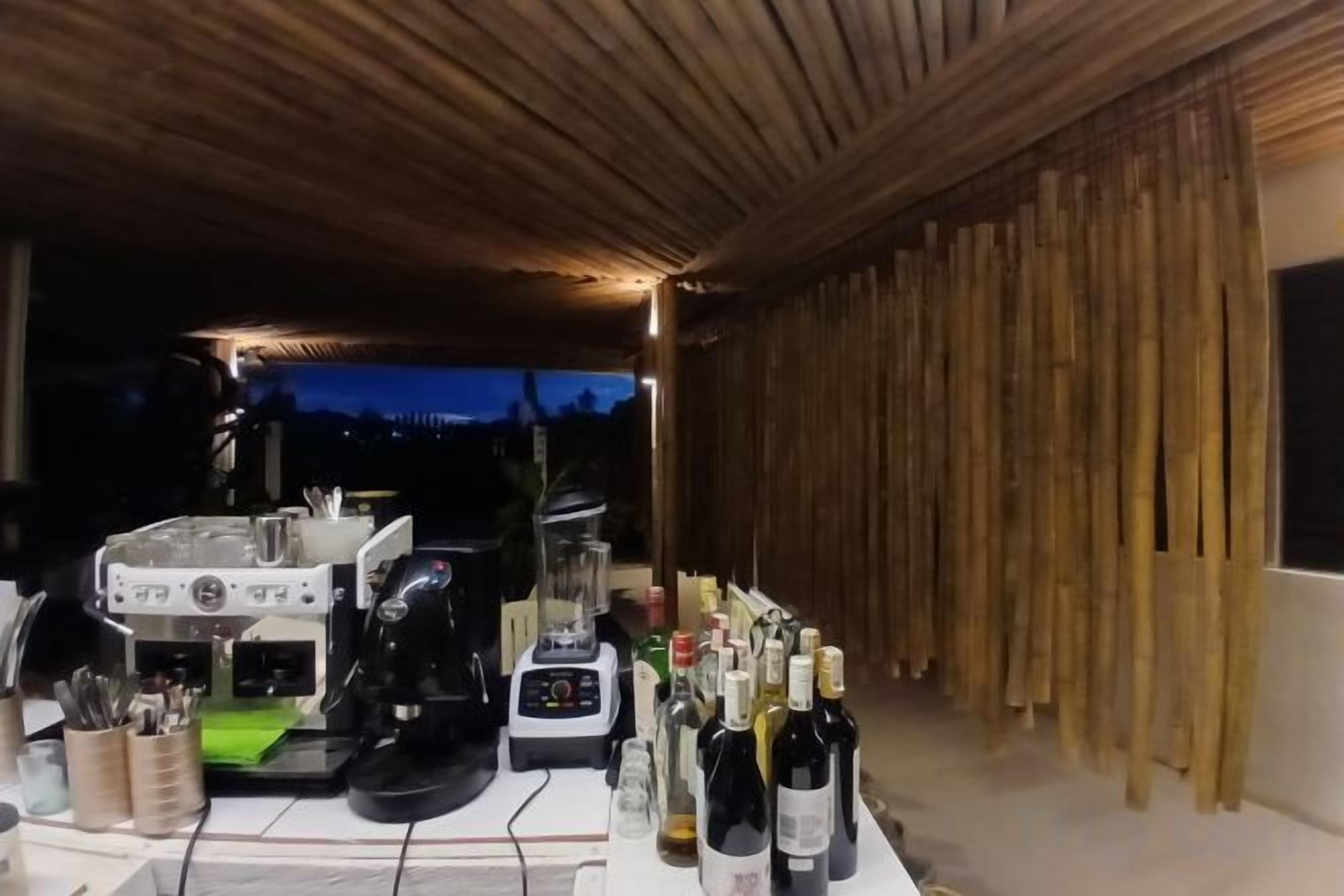 A covered outdoor area with a bar setup including a blender and a coffee machine, and a variety of bottles.