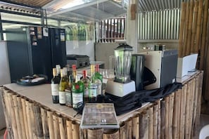 A bar area with a counter, bottles, a blender, and a refrigerator.