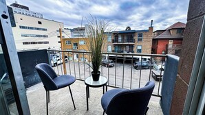 Ein Balkon mit zwei Stühlen und einem kleinen Tisch, mit Blick auf einen Parkplatz und Gebäude.