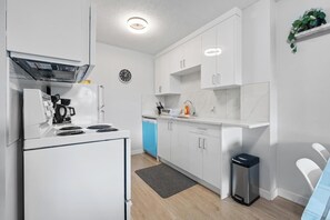 A modern kitchen with white cabinets, a built-in oven, a dishwasher, and a clock on the wall. - Walk Score 95, City Views, Free Parking & Wifi (Calgary)