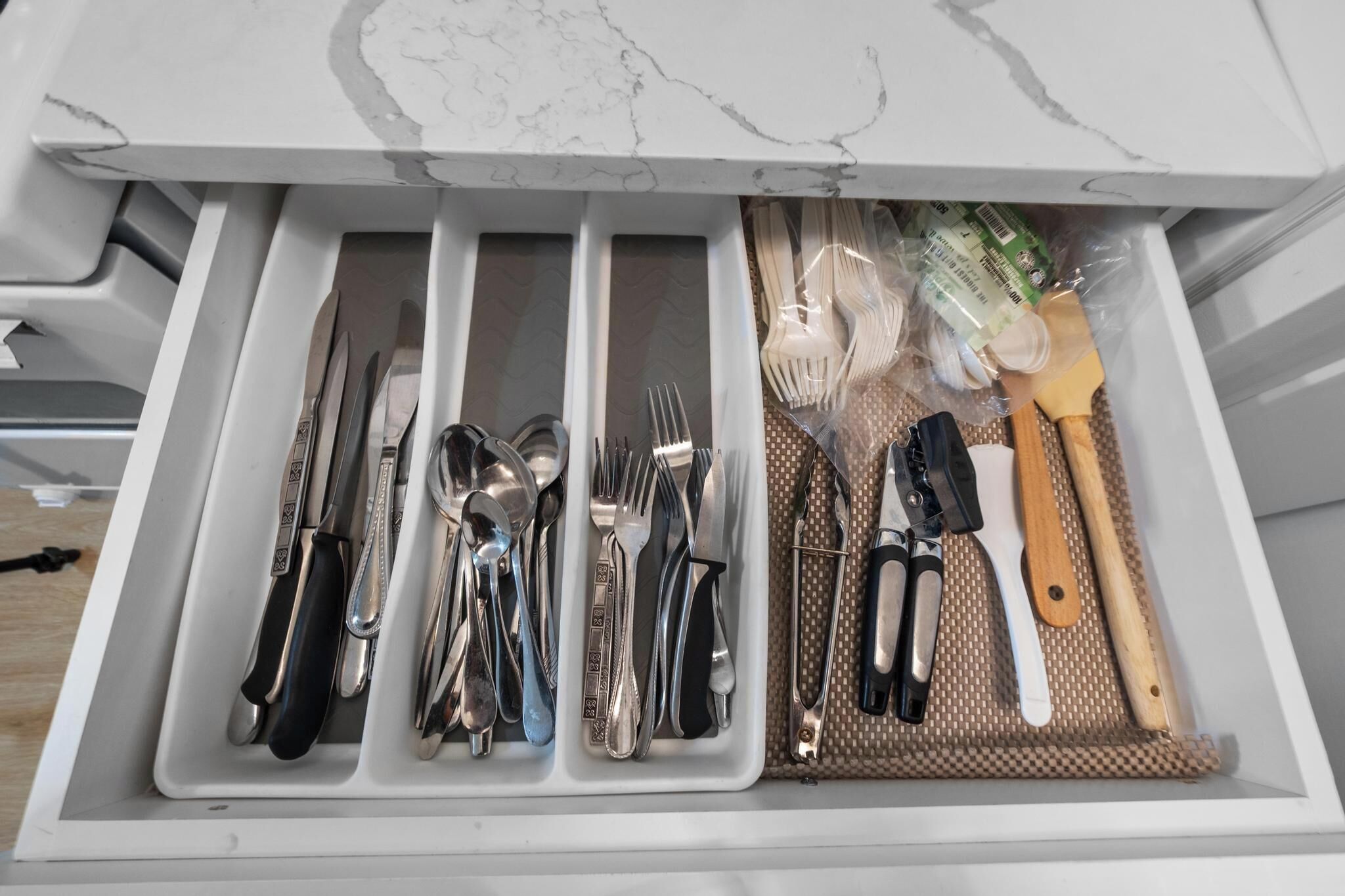 A drawer with neatly organized kitchen utensils including knives, spoons, forks, and a spatula.