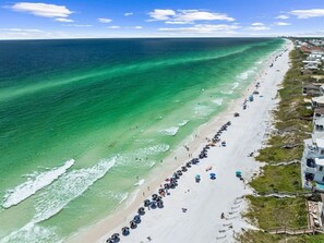 An aerial view of a beach with a long stretch of umbrellas and beachgoers.