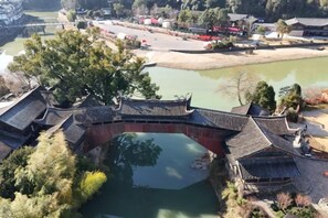 A traditional Chinese-style bridge over a pond with a view of a park and buildings in the background. - Qiaopan Guesthouse (Taishun)