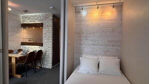 A compact room with a bed, a dining area with a table and chairs, and a stone accent wall.