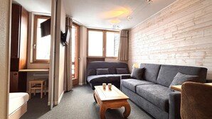 A cozy living room with a grey sofa, a wooden coffee table, and a TV mounted on the wall.