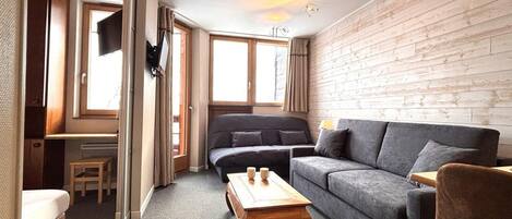 A cozy living room with a grey sofa, a wooden coffee table, and a TV mounted on the wall.