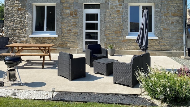 A stone house with a pitched roof, a wooden patio with outdoor furniture, and a barbecue grill. - Maison en Pierre (Ploumagoar)