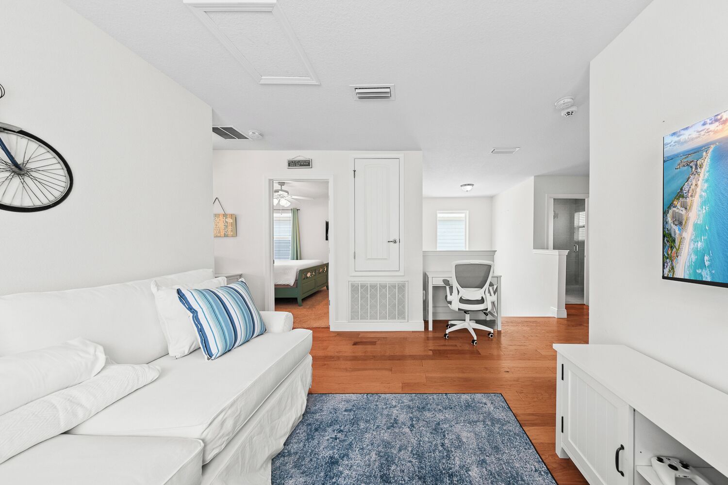 A spacious living area with a white sofa, a blue rug, and a large window.