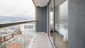 A modern balcony with a glass door leading to a bedroom. The balcony overlooks a cityscape with buildings and mountains in the distance. - Uhaus 704 (Manizales)