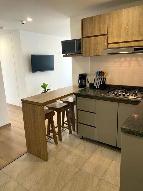 A modern kitchen with wooden cabinets, a microwave, a gas stove, and a coffee maker. - Uhaus 704 (Manizales)