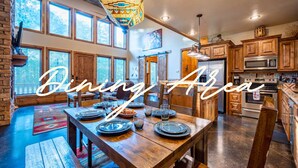 A dining area with a wooden table set for four, a hanging light fixture, and a kitchen in the background. - Woodland Family Retreat Near the Lake (Broken Bow)
