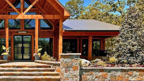 A wooden lodge with a steep gabled roof, a stone entrance, and a covered porch. - Woodland Family Retreat Near the Lake (Broken Bow)