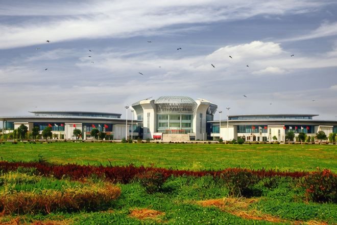 A modern building with a central dome and two wings, surrounded by a green field.