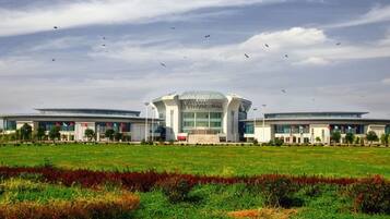A modern building with a central dome and two wings, surrounded by a green field.