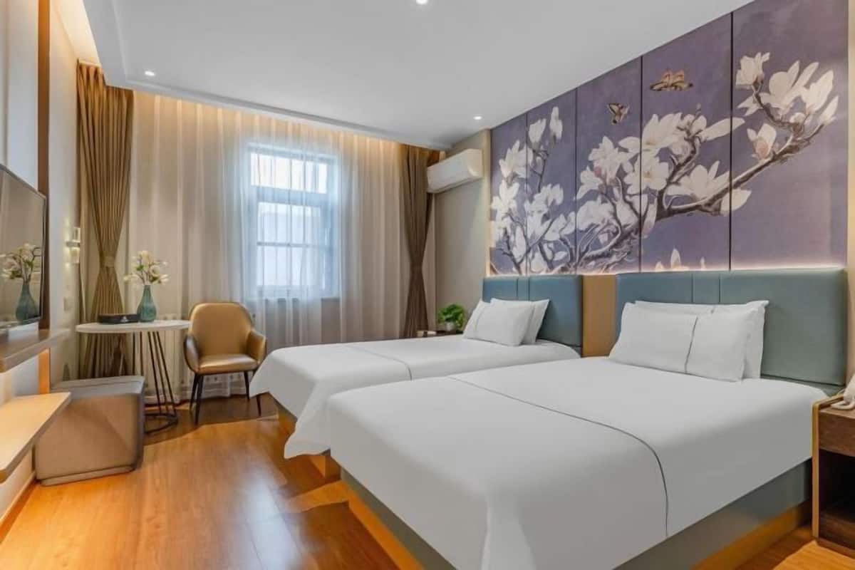 Une chambre d’hôtel avec deux lits, un bureau, une chaise, une fenêtre avec des rideaux et une œuvre d’art accrochée au mur.