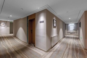 A hotel corridor with a carpeted floor, a wooden door, and a framed sign on the wall. - Magnotel Hotel (Qufu Sankong Scenic Area Chunqiu West Road) (Qufu)