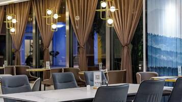 A restaurant with tables and chairs, curtains, and hanging lights.