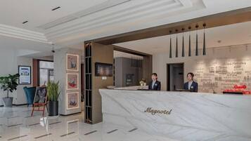 A hotel reception area with a marble counter, framed artwork, and a seating area with a plant.