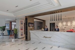 A hotel reception area with a marble counter, framed artwork, and a seating area with a plant. - Magnotel Hotel (Qufu Sankong Scenic Area Chunqiu West Road) (Qufu)