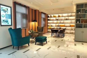 A modern hotel lobby with a seating area, a dining table, and a bookshelf. - Magnotel Hotel (Qufu Sankong Scenic Area Chunqiu West Road) (Qufu)