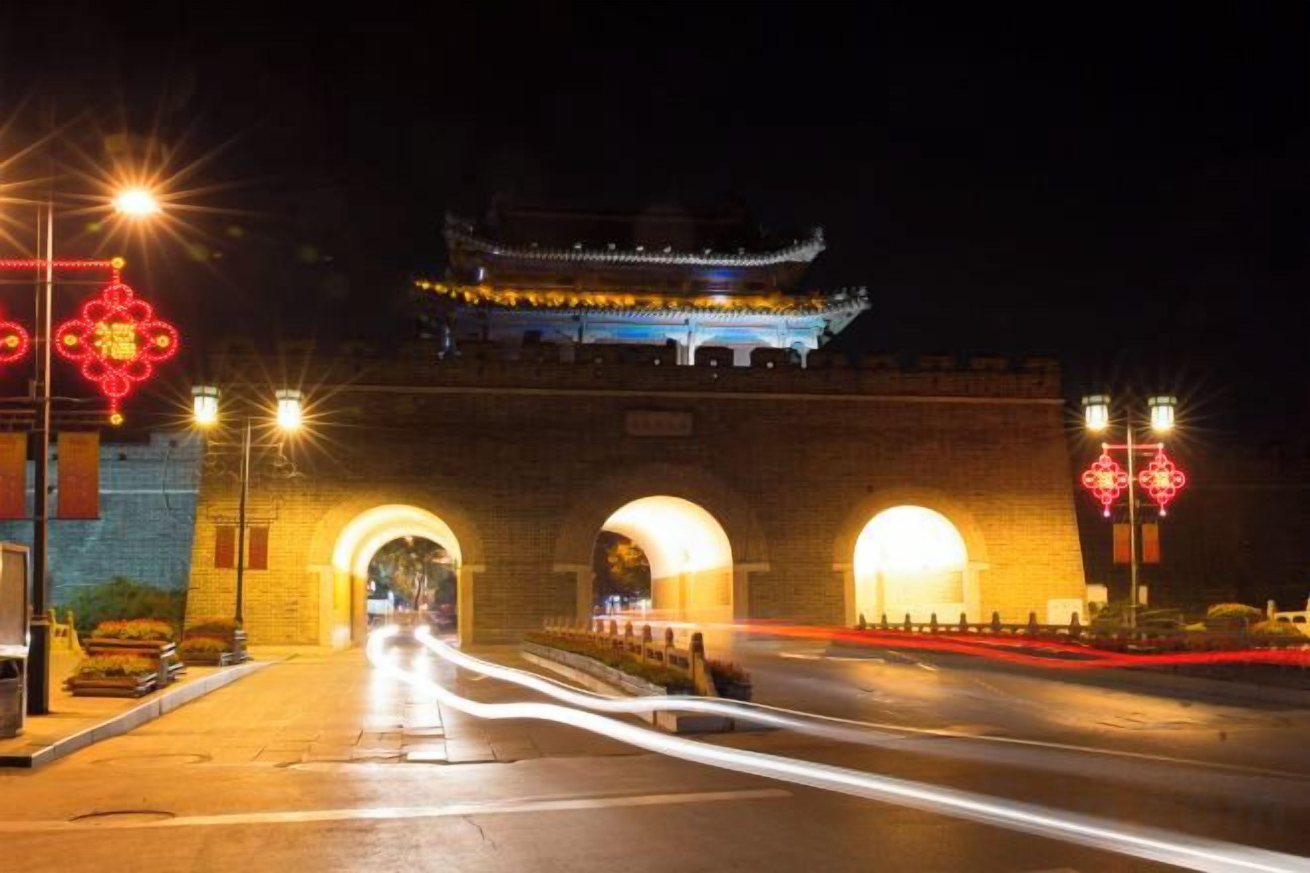 Una puerta tradicional china de noche, con arcos iluminados y una pagoda al fondo.