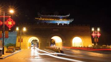 Una puerta tradicional china de noche, con arcos iluminados y una pagoda al fondo.