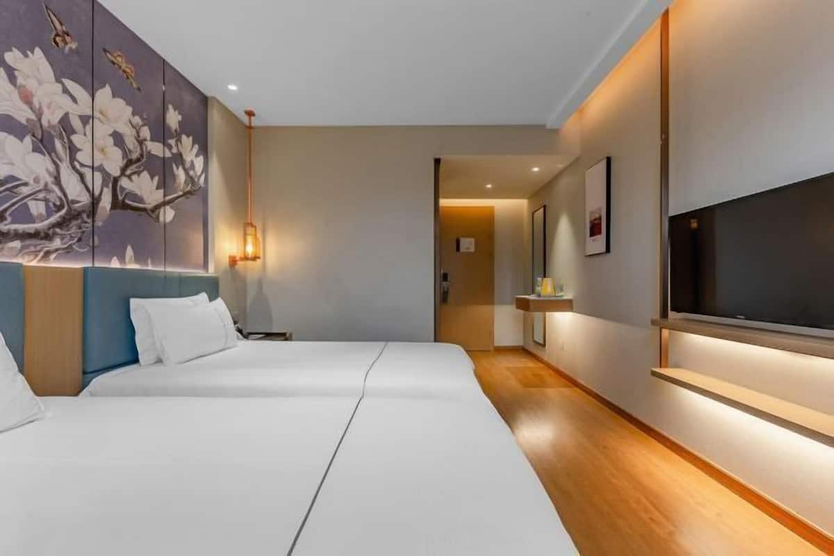Une chambre d’hôtel avec deux lits, un grand téléviseur fixé au mur et un tableau représentant des fleurs.