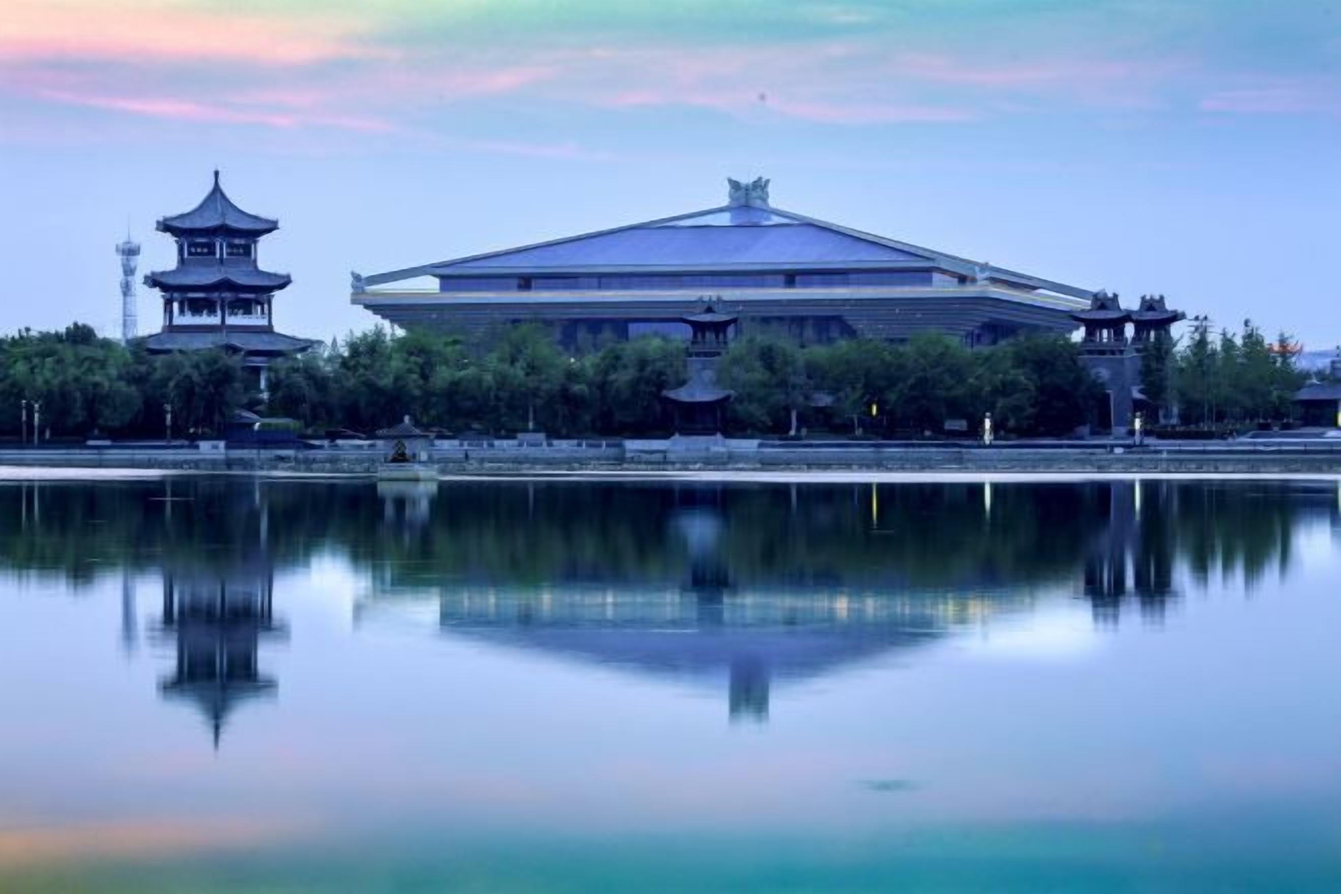 A traditional building with a pagoda-style tower and a large, modern structure across a reflective water body.