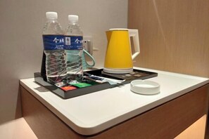 Un mini-bar d’hôtel contenant deux bouteilles d’eau, une machine à café et un plateau avec divers articles.