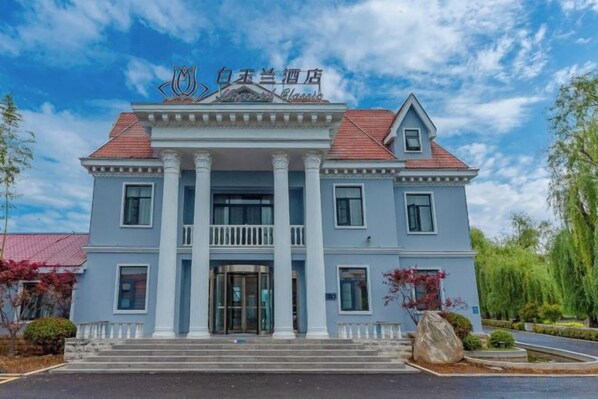 A two-story building with a symmetrical facade, a central entrance with a balcony, and a red-tiled roof. - Magnotel Hotel (Qufu Sankong Scenic Area Chunqiu West Road) (Qufu)