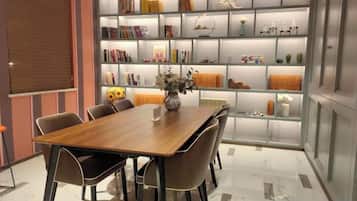 A modern dining area with a wooden table and chairs, a bookshelf with various items, and a decorative vase.
