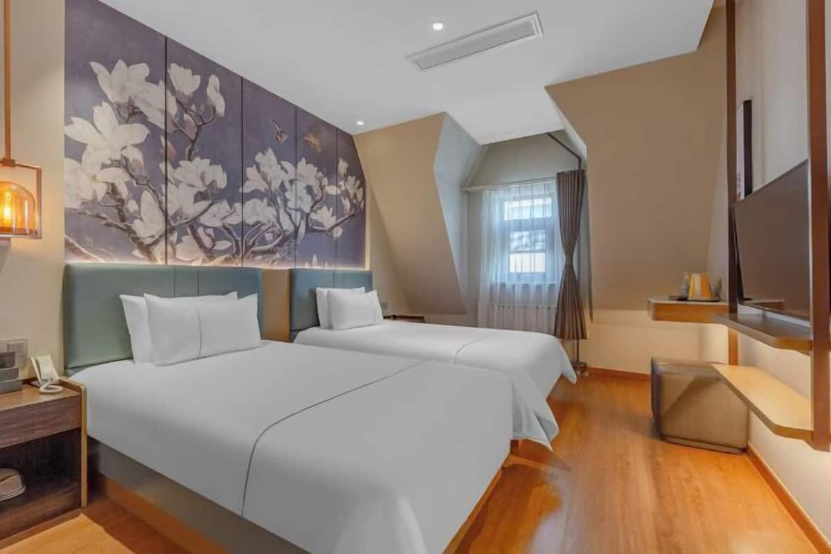 Une chambre d’hôtel avec deux lits, une grande œuvre d’art florale au mur, une télévision et un plancher en bois.